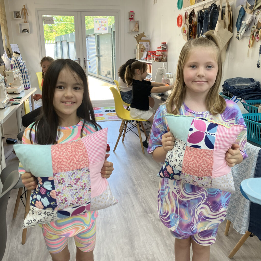 2 children showing the cushions they have made at sewing lessons in Tameside